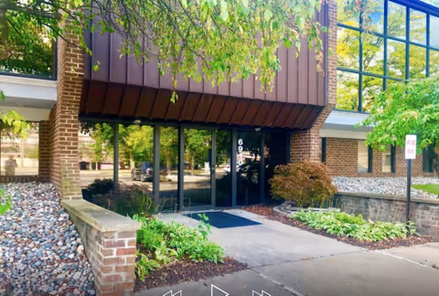 Entrance to a brick senior living facility with glass doors and landscaping.