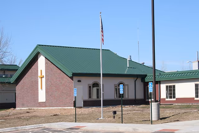 Exterior view of Guardian Angels Health & Rehab Center with green roof and cross on wall.