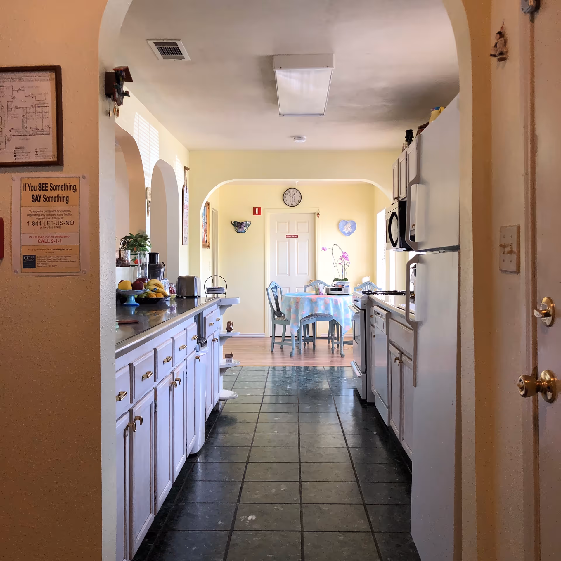Long kitchen corridor with white cabinets, appliances, and a dining area beyond arches.