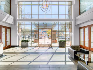Bright lobby with floor-to-ceiling glass entrance, seating area, and potted plants.