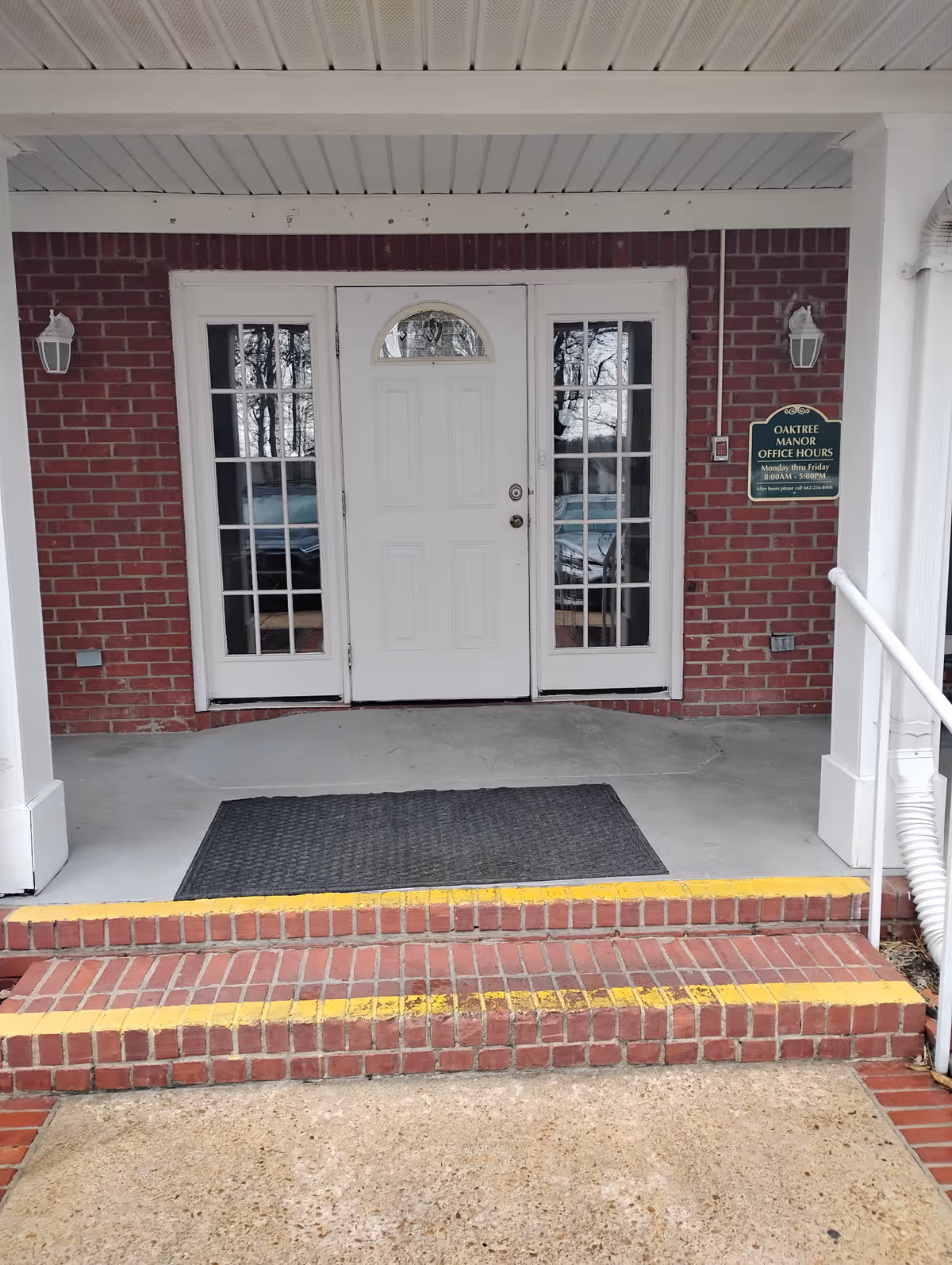 Brick building entrance with white doors and a covered porch; Oak Tree Manor sign nearby