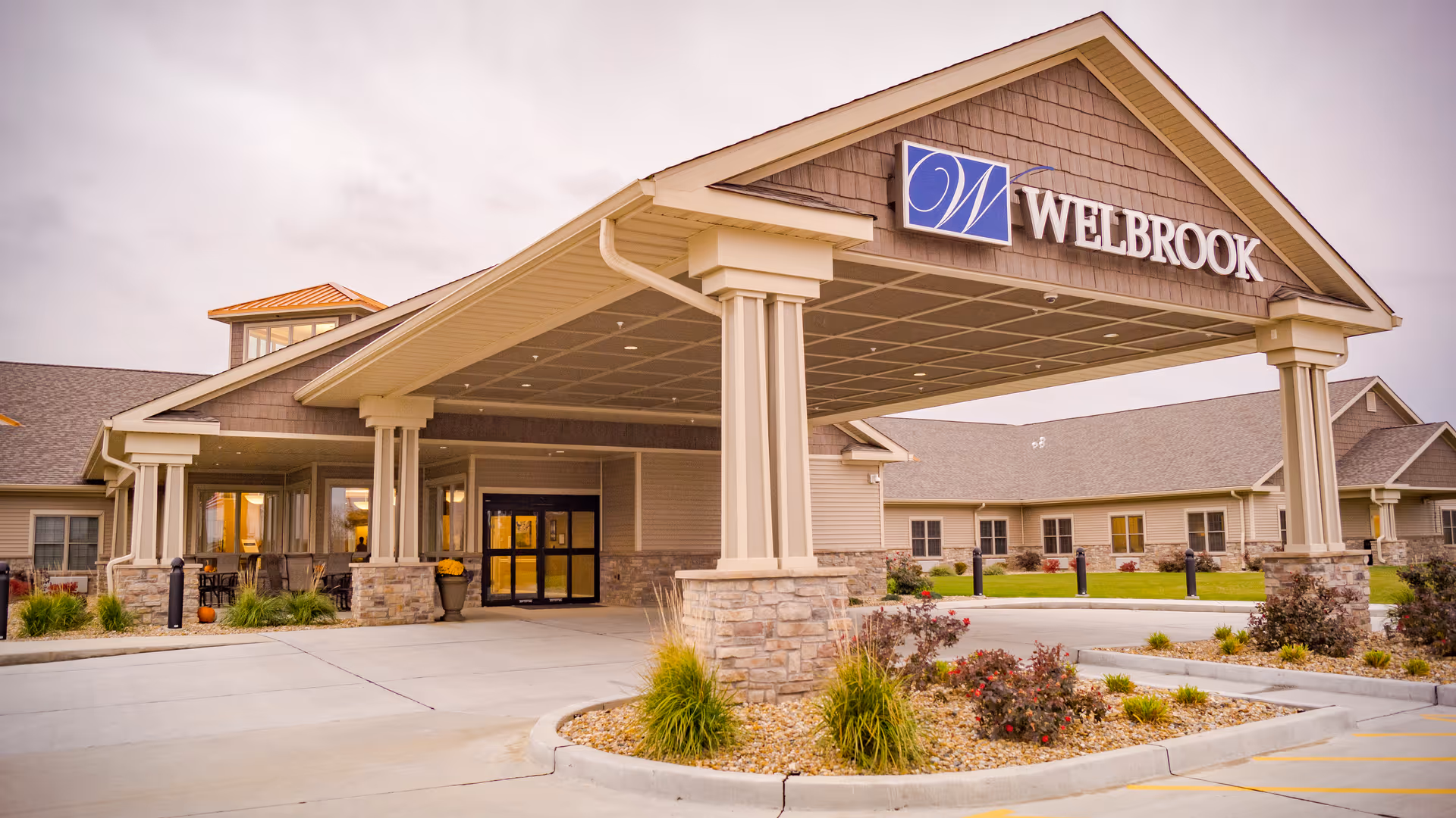 Exterior view of a senior living facility entrance with a covered drop-off and landscaping.