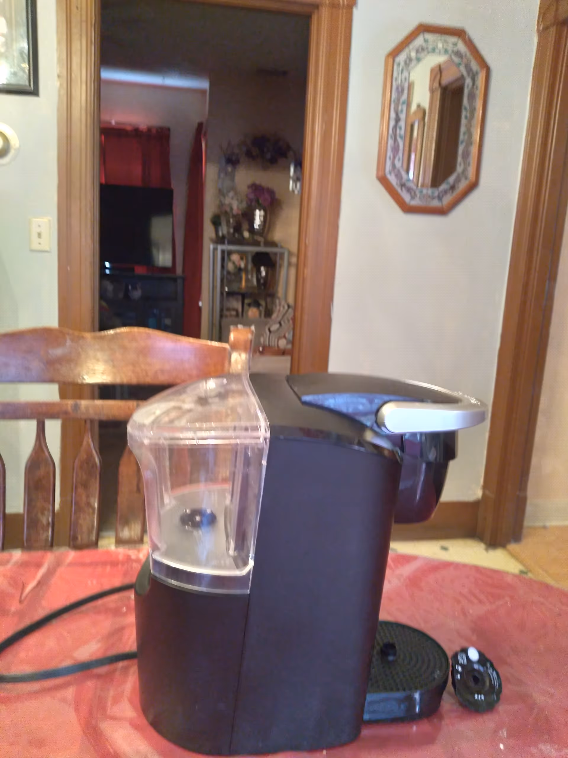 Black coffee maker sits on a dining table in a cozy home interior.