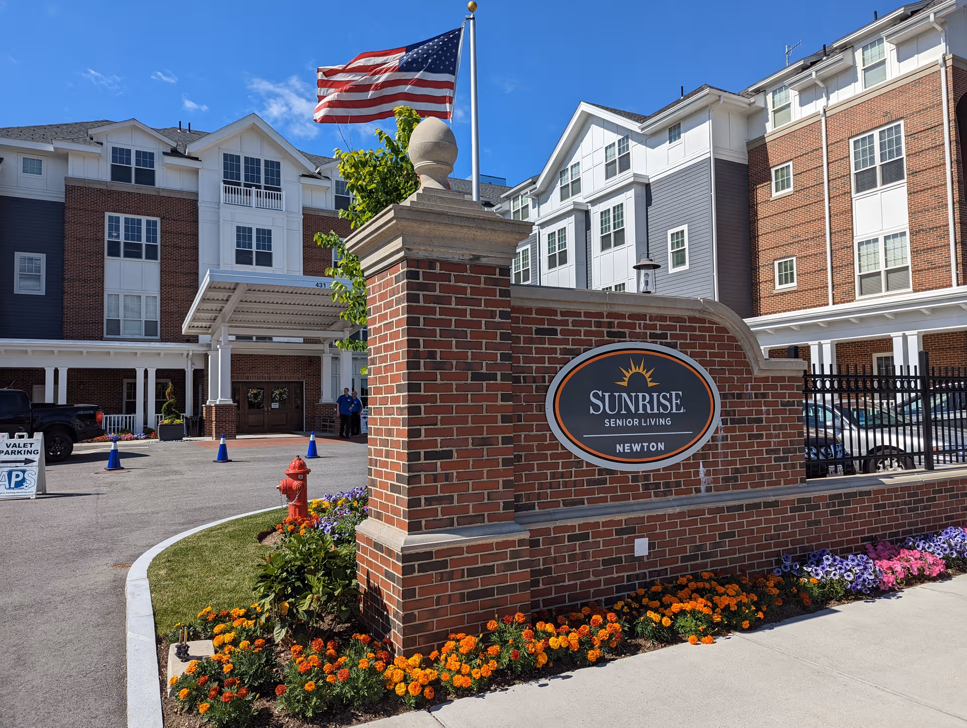 Brick Sunrise Senior Living Newton entrance sign with flag and colorful flowers.