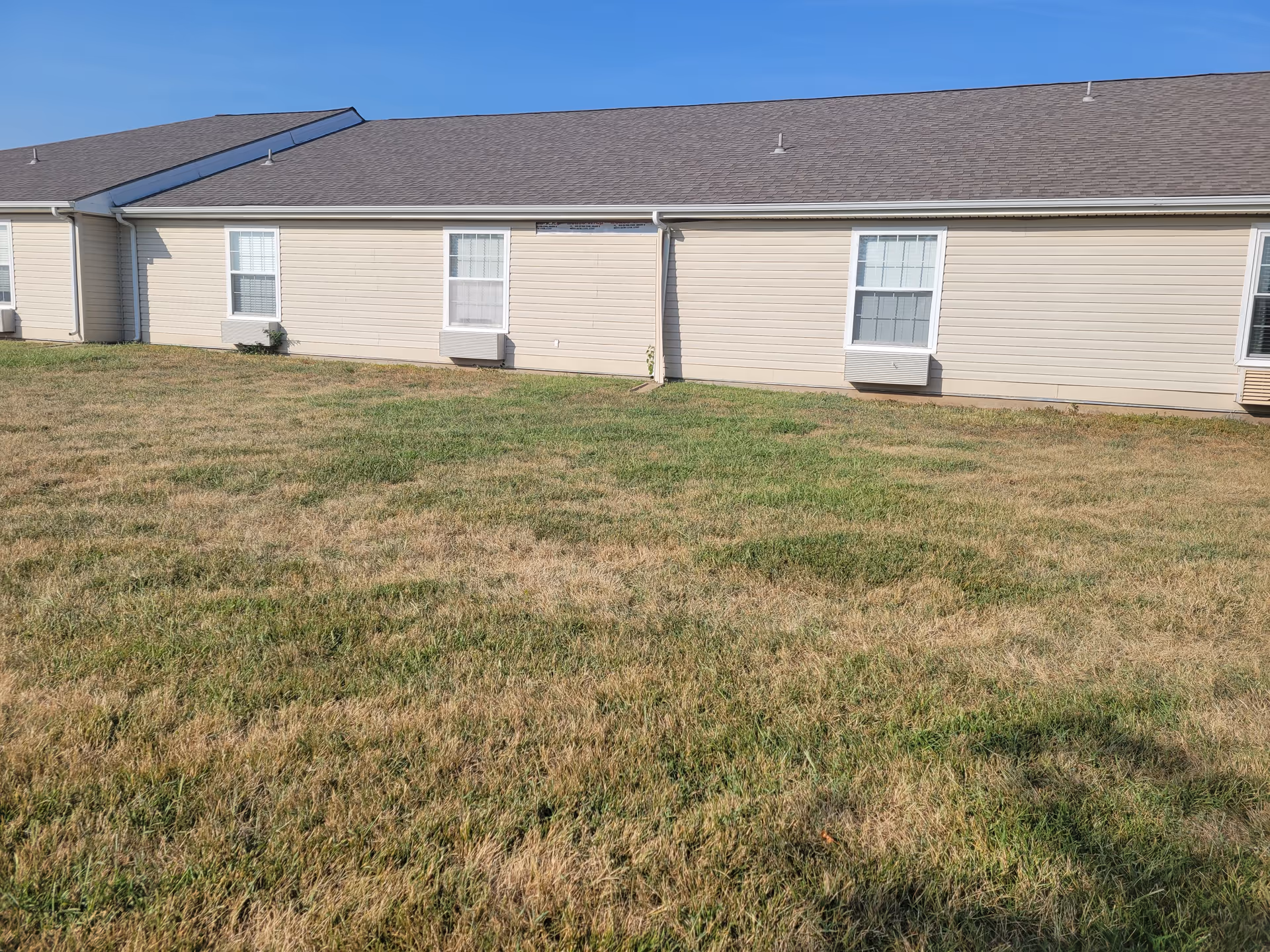 Single-story beige senior living facility exterior with windows and a grassy lawn in front.