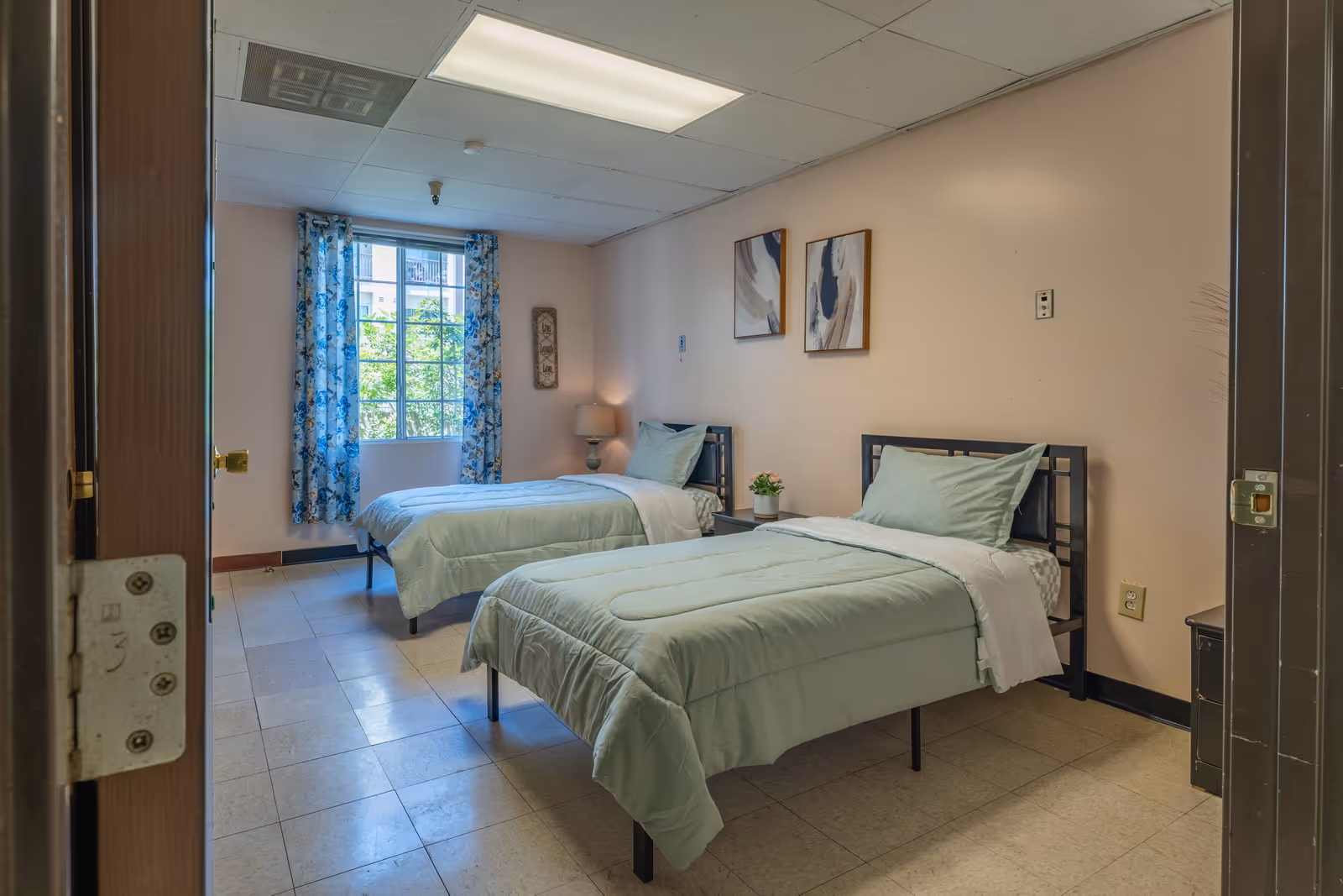 Two twin beds with mint green bedspreads in a shared senior living bedroom.
