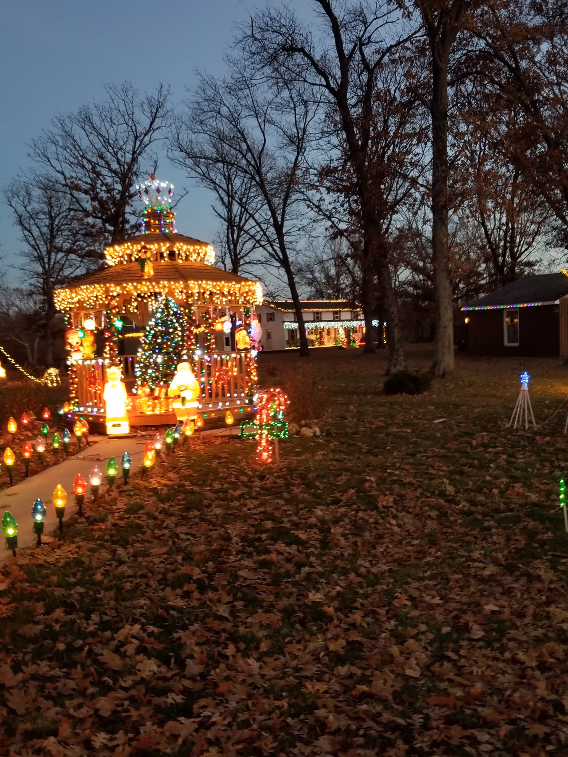 Outdoor holiday lights illuminate a gazebo shaped structure and a lit garden path.
