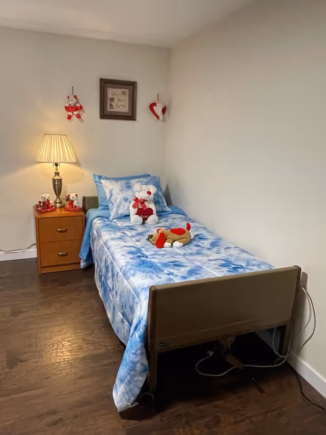 Single bed with blue tie-dye bedding, stuffed animals, and a nightstand in a small bedroom.