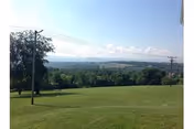 Expansive grassy lawn with distant hills, trees, and utility poles under a clear blue sky.