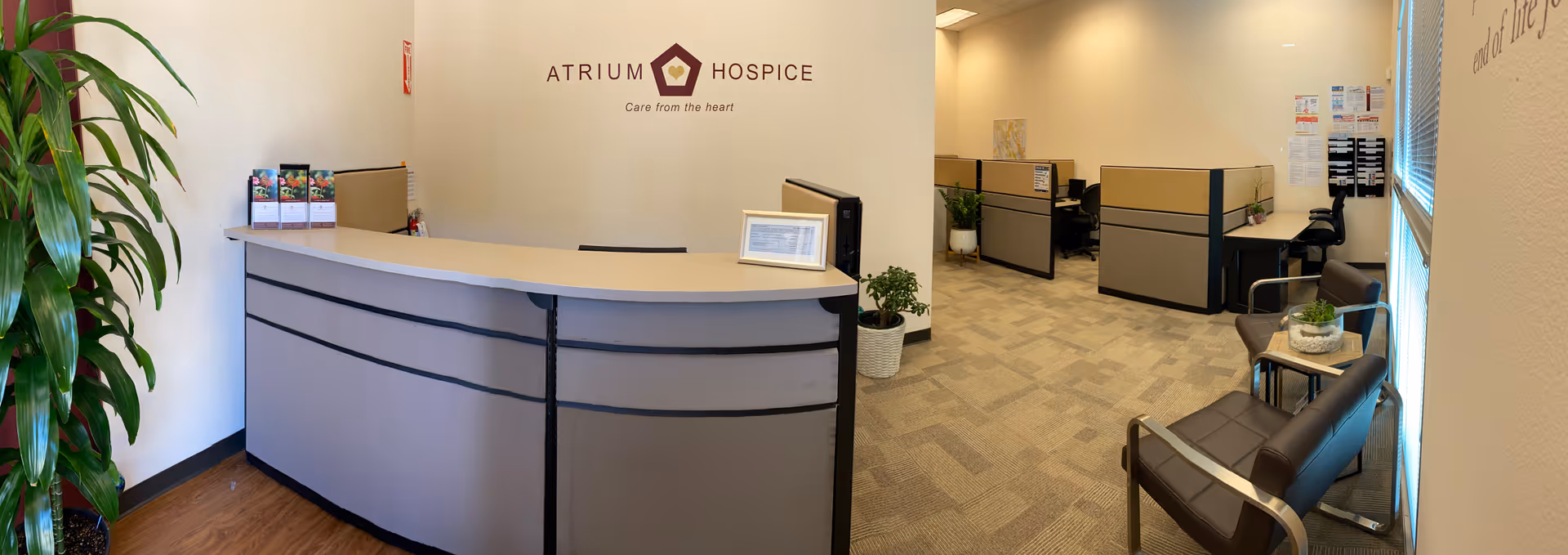Lobby reception area with curved front desk, seating, cubicles, and Atrium Hospice signage
