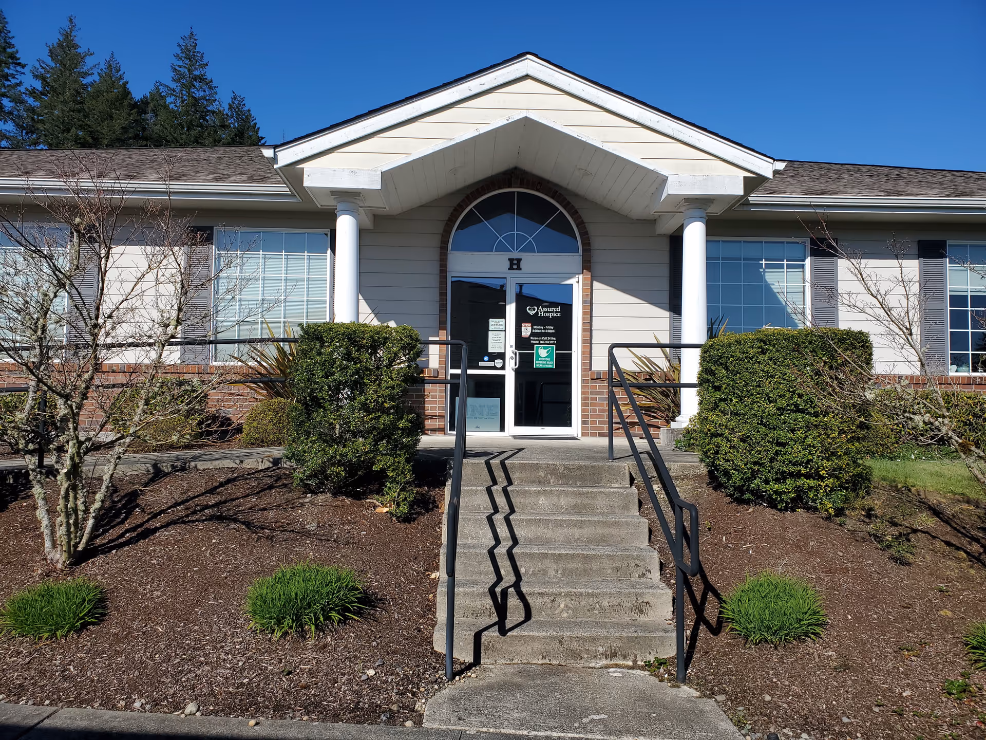 Front view of a single-story facility entrance with stairs, columns, and landscaped shrubs.