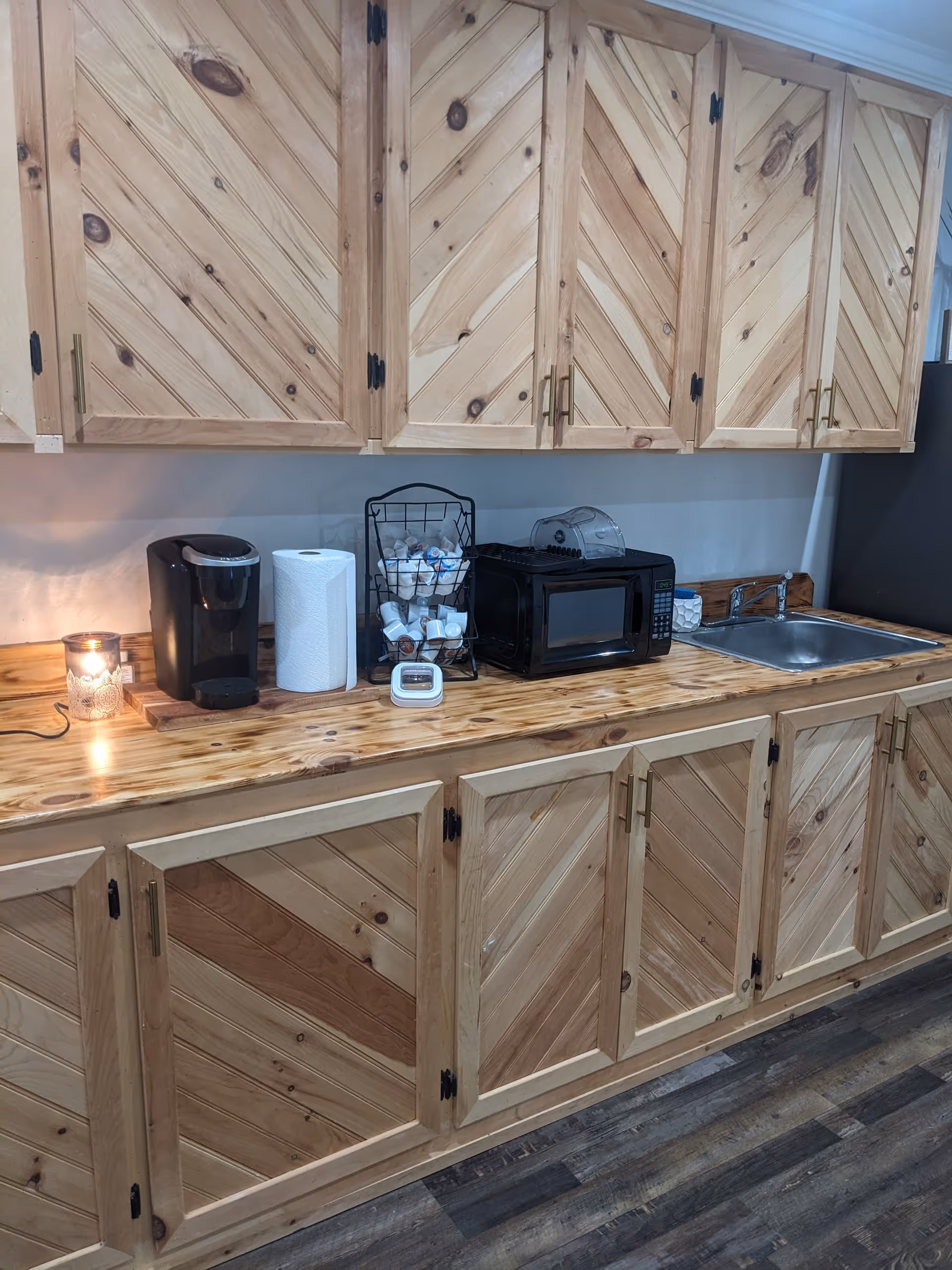 Wood-paneled kitchenette with coffee maker, microwave, toaster rack, sink, and paper towels.