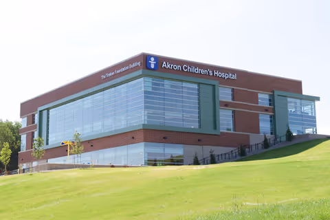 Brick Akron Children's Hospital building with expansive glass windows atop a grassy slope.