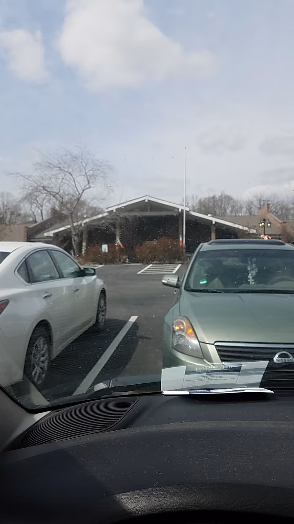 View from inside a car of the building entrance and parked cars in the lot
