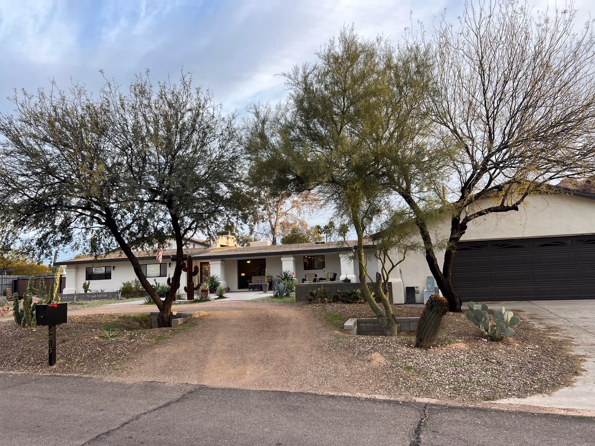 A single-story adult living facility with a two-car garage, desert landscaping, and front yard trees.