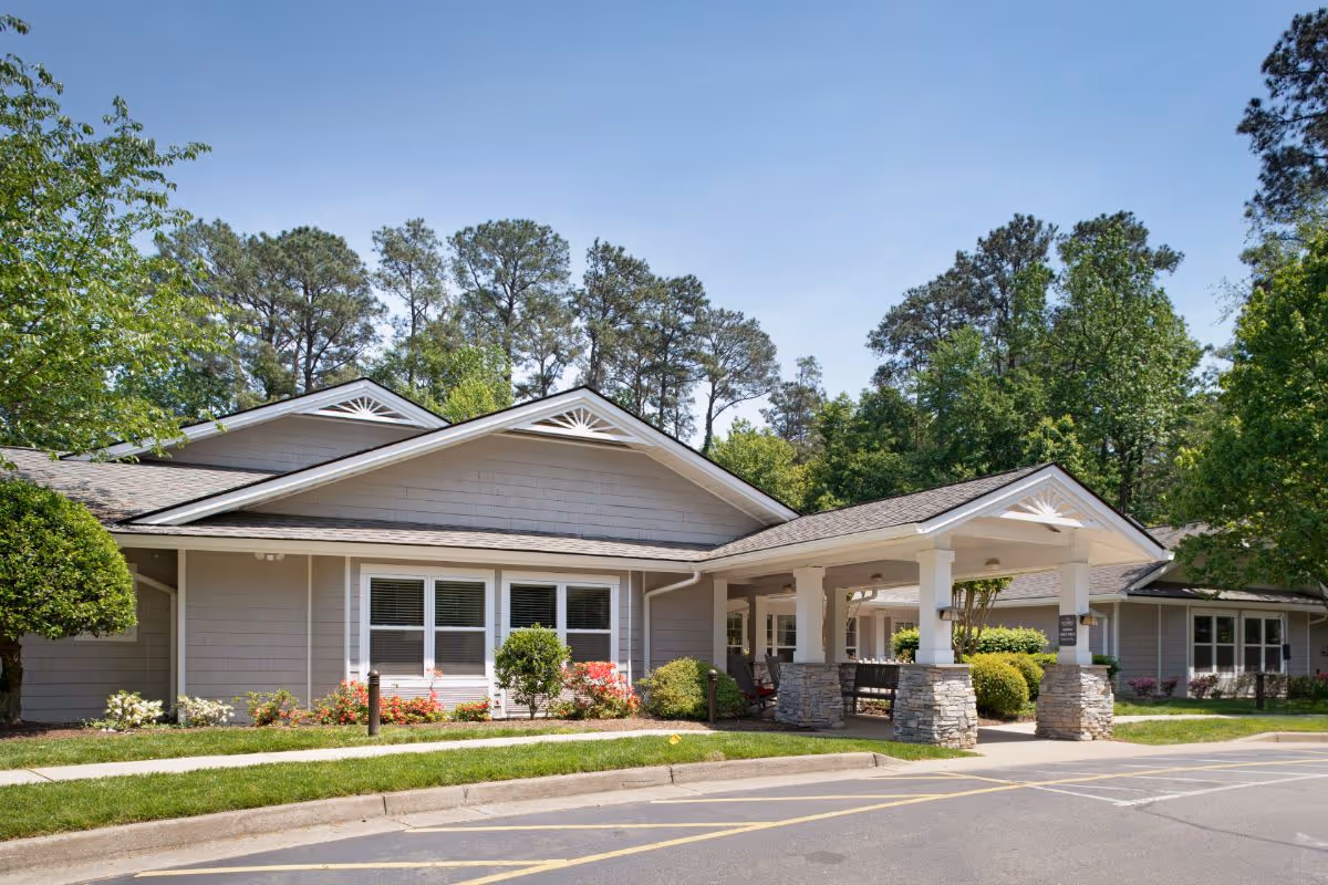 Single-story senior living facility with a covered entrance supported by stone columns, manicured landscaping and trees in front.