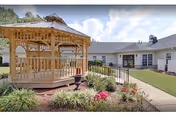 Wooden gazebo in a landscaped courtyard with a single-story building in the background.
