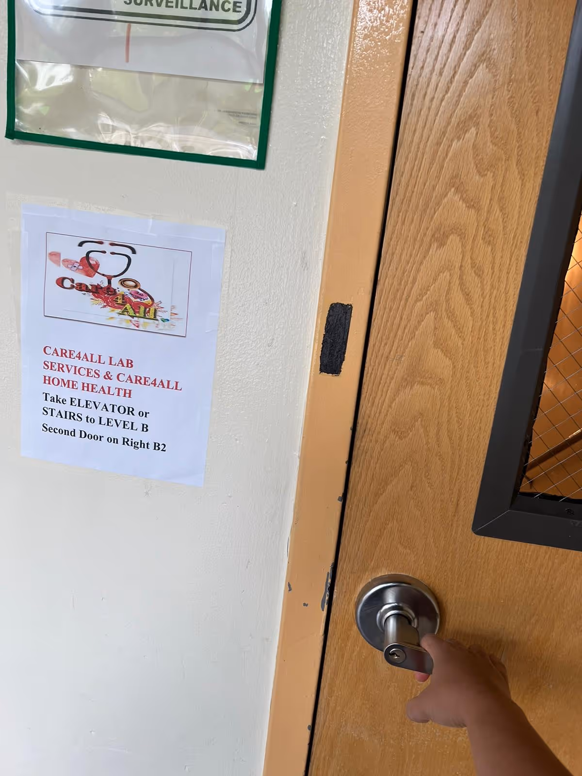 Hand on door knob beside wall with Care4All Lab Services sign in interior hallway.