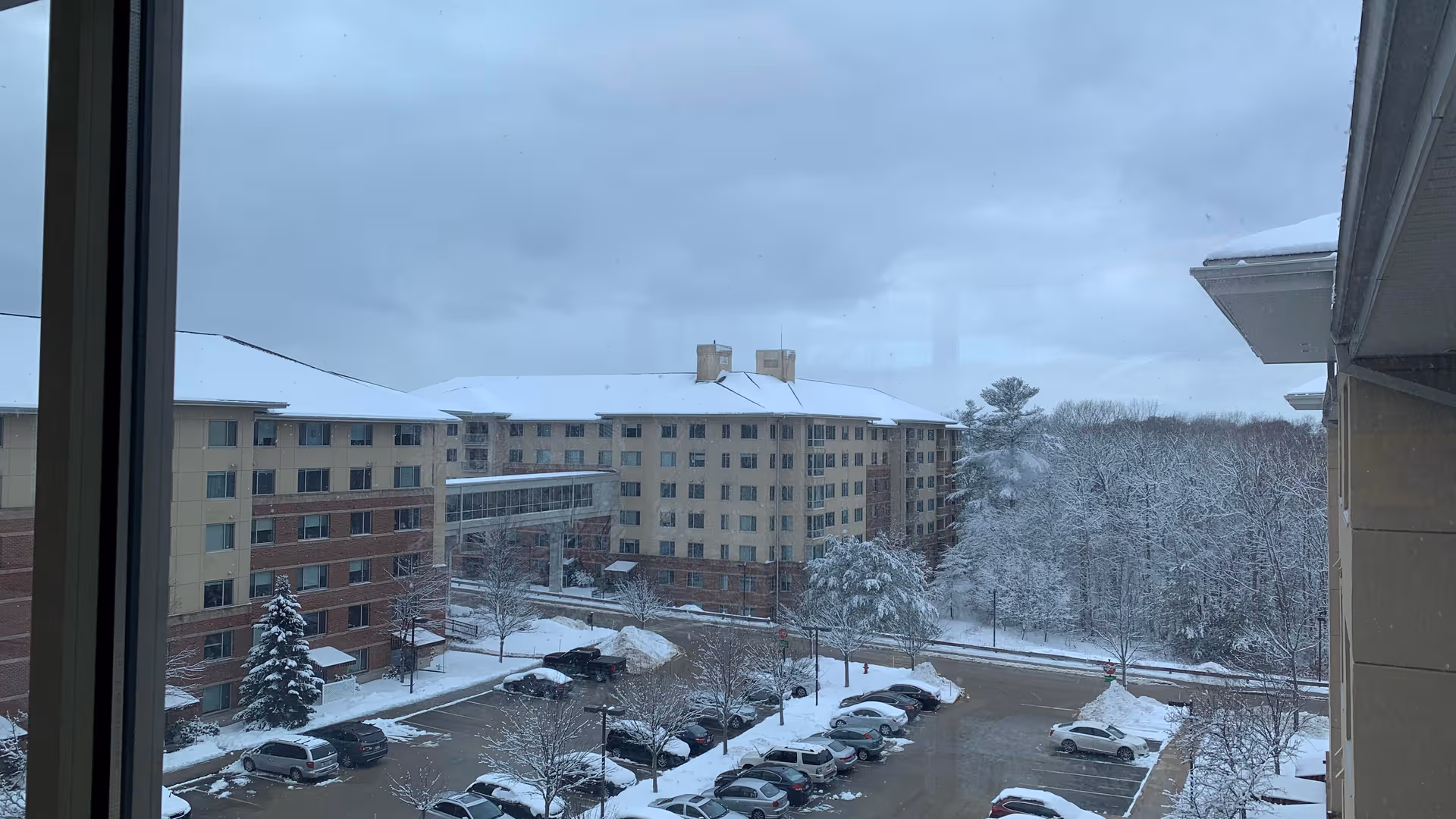 Snowy senior living campus with beige buildings, trees, and a parking lot outside Linden Ponds.