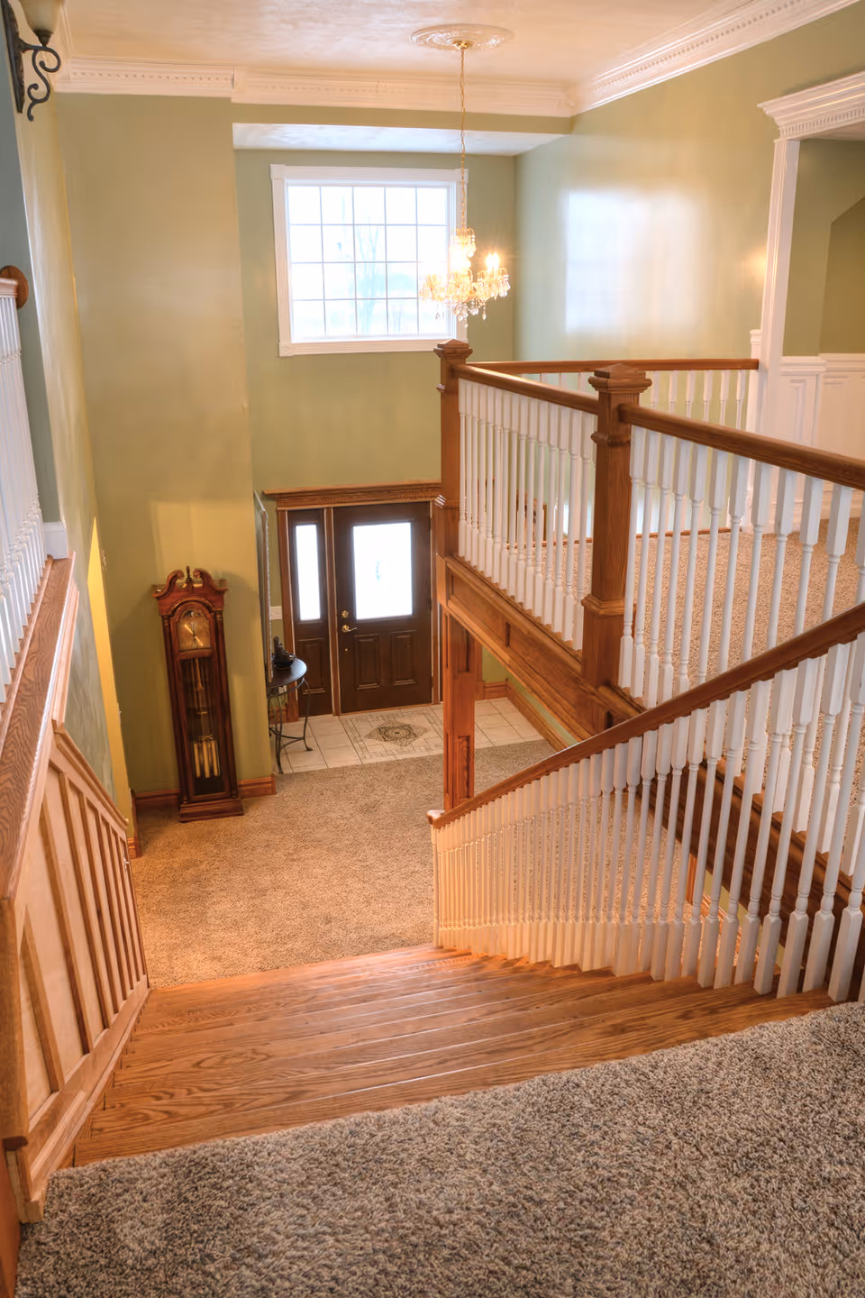 Two-story foyer with green walls, staircase, chandelier, and front entry door.