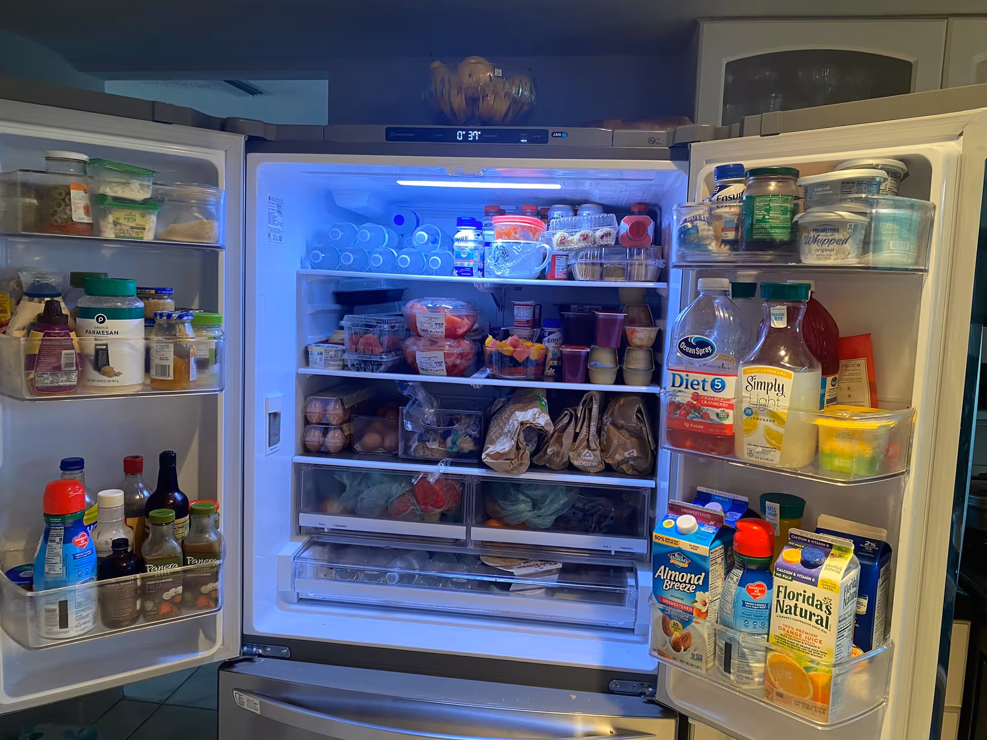 Open refrigerator in a senior living facility kitchen, filled with food, drinks, and condiments.