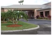 Front view of a single-story facility entrance with a circular landscaped island and palm trees.