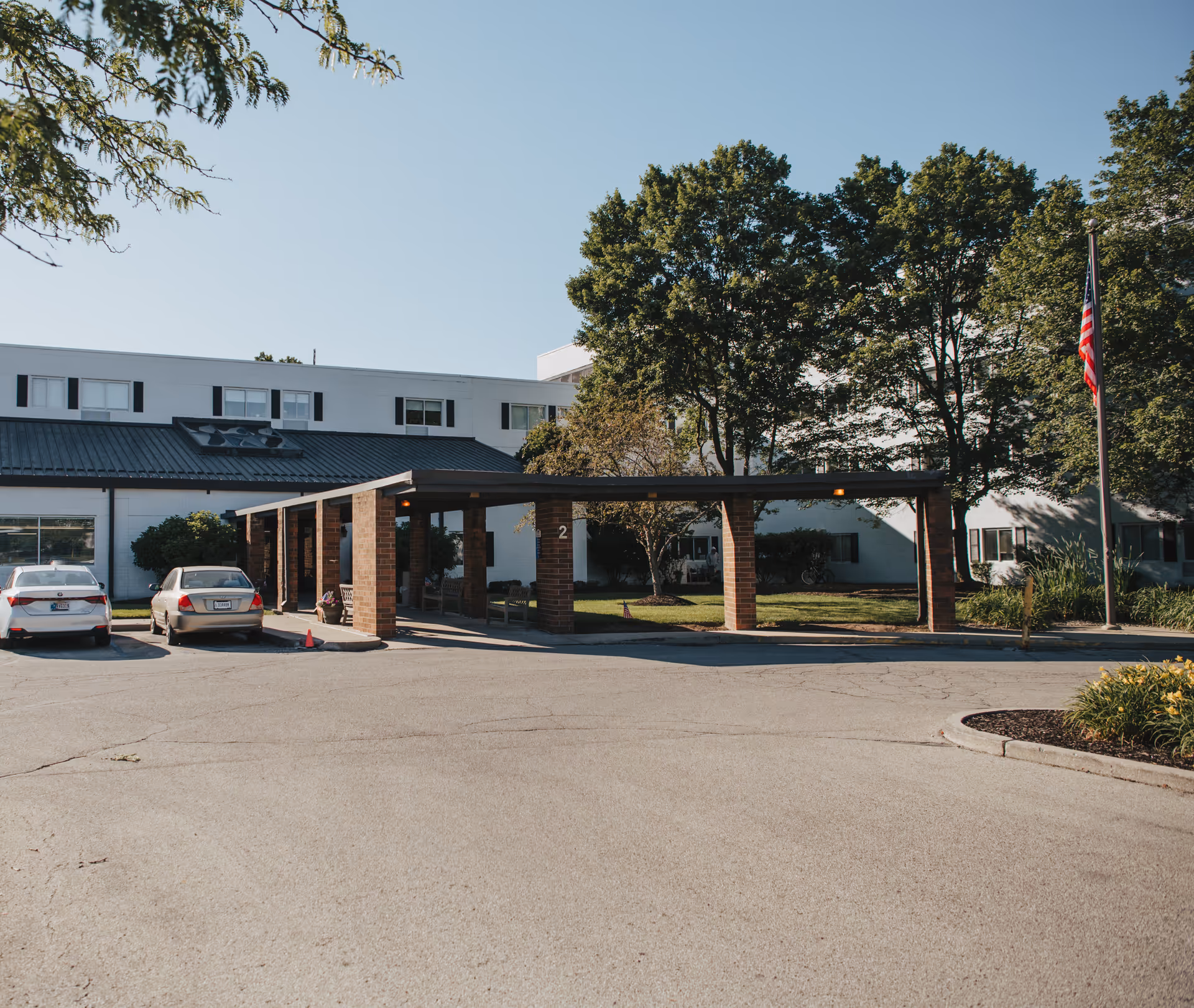 Exterior view of Majestic Care of Carmel with a covered entrance, cars, and flag.