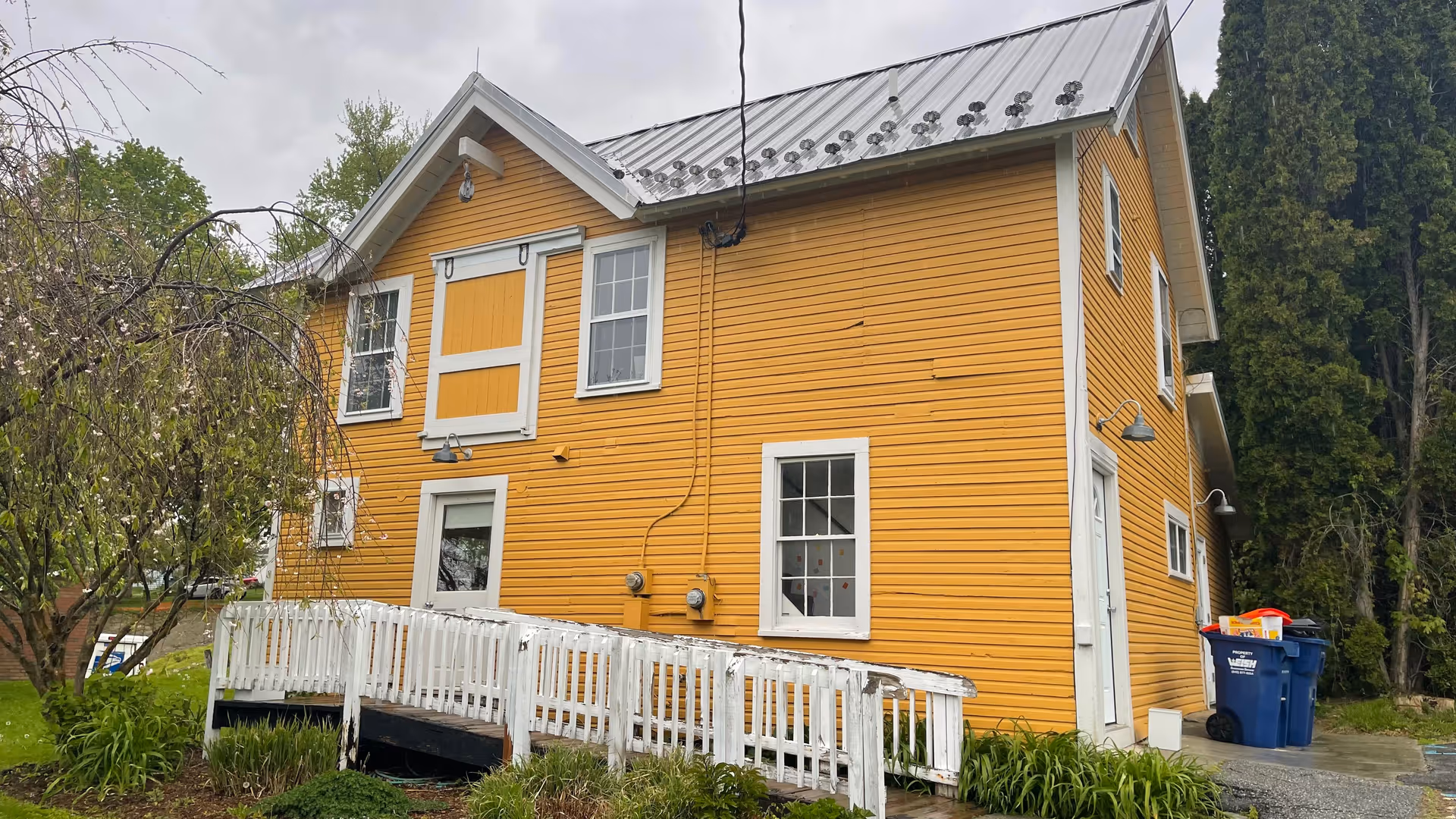 Yellow wooden building with white trim, metal roof, and a white railing deck.