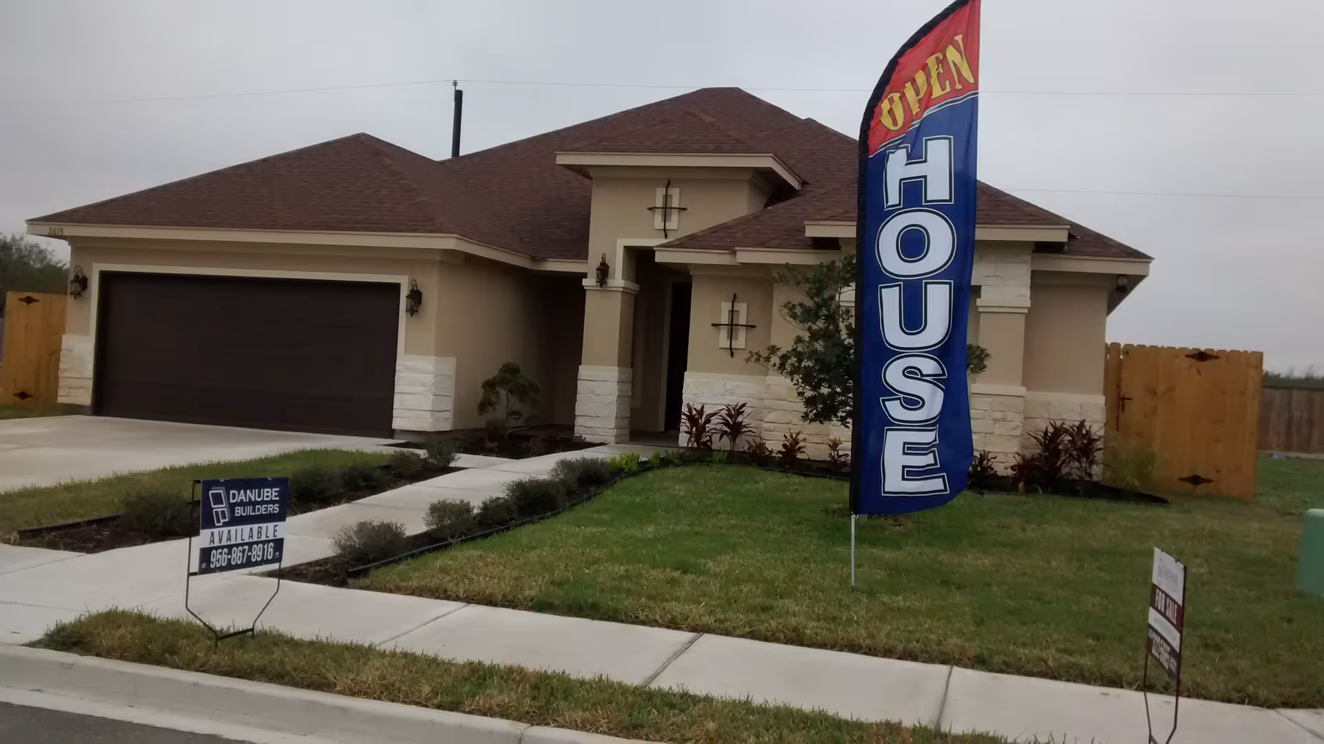 Beige single-story house with an open-house flag and manicured front lawn.