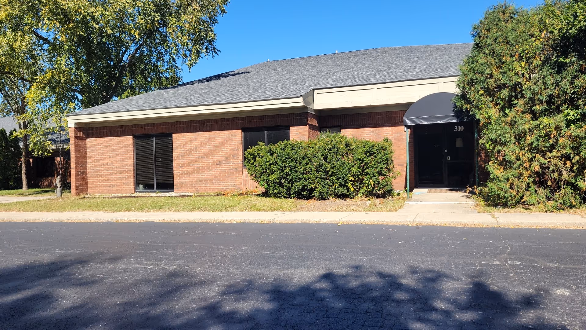 Brick senior living facility exterior with a black entrance awning and surrounding shrubs.