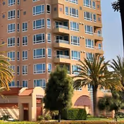 Tall peach-colored senior living building with balconies and palm trees in front.