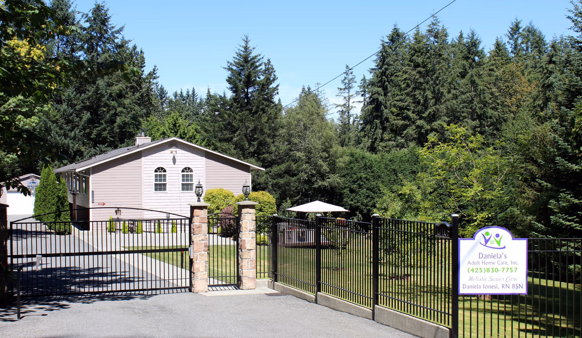 Gated entrance to Daniela's Adult Home Care, Inc., with a light building and surrounding greenery.