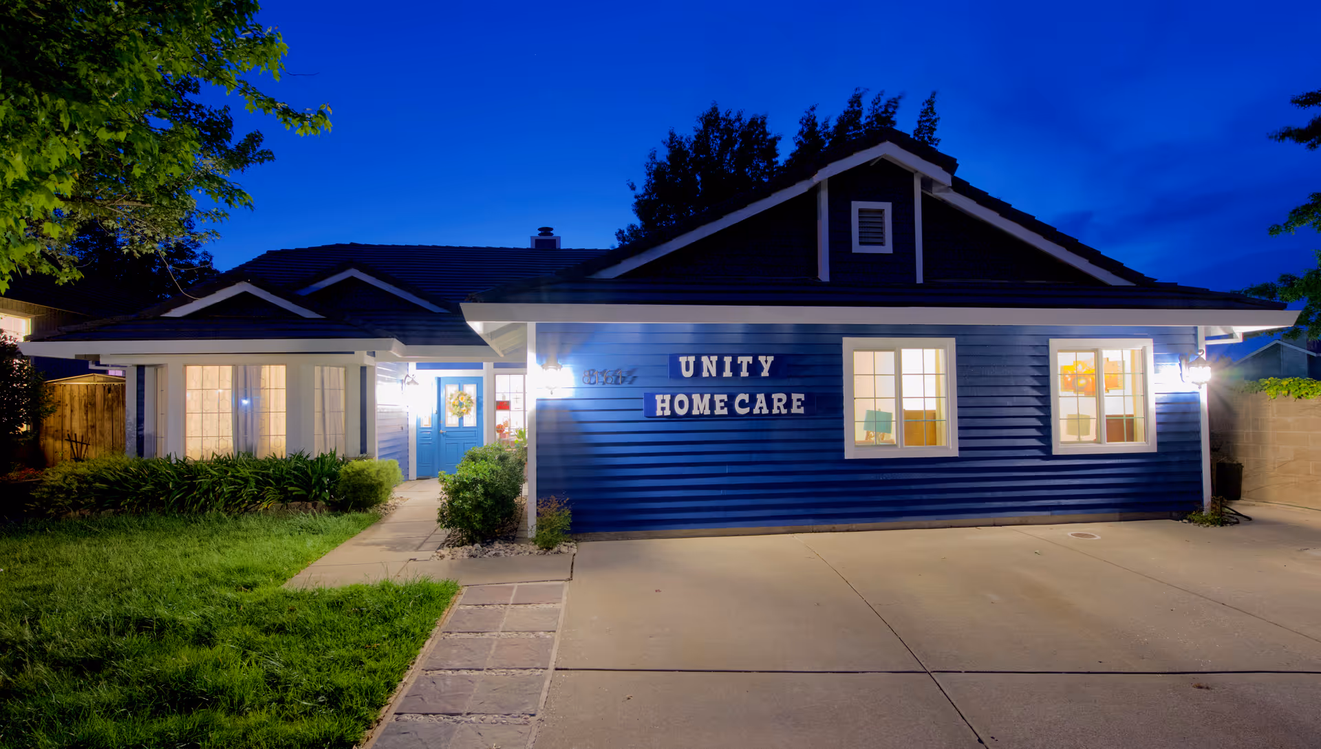 Blue single-story building with Unity Home Care sign at night, entrance lit.