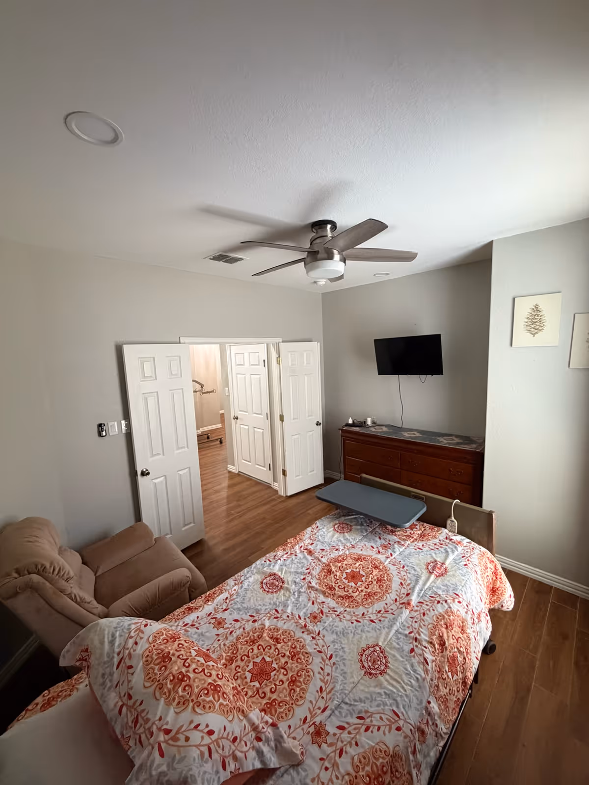 Bedroom with bed, quilt, recliner, dresser, and wall-mounted TV.