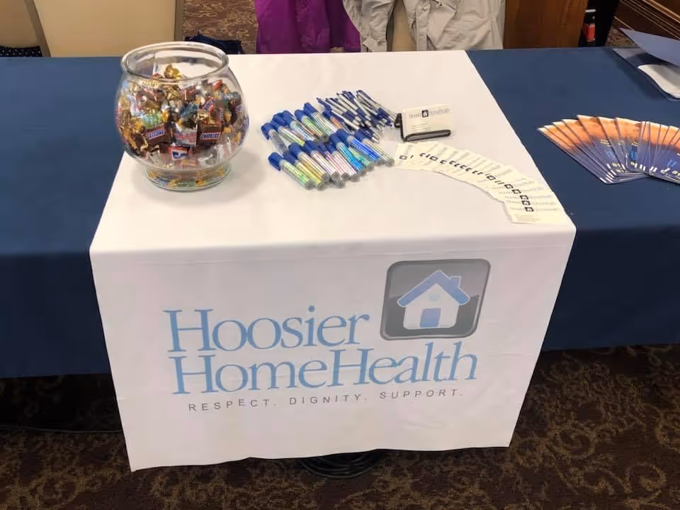 Promotional table with Hoosier Home Health banner, candy jar, pens, and brochures.
