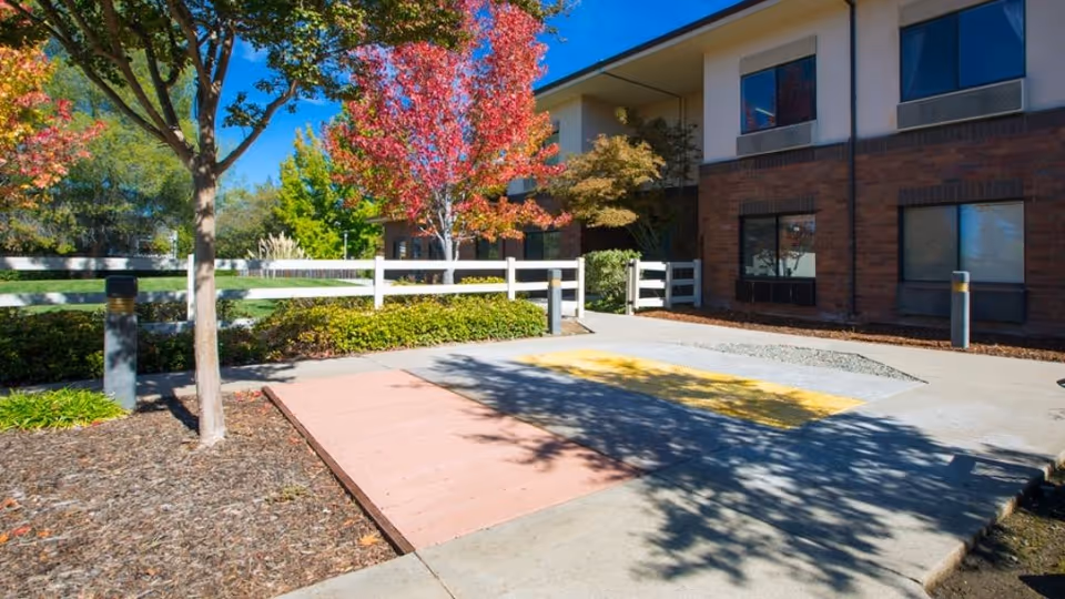 Exterior view of Manorcare Health Services Citrus Heights with trees, walkway, and white fence.