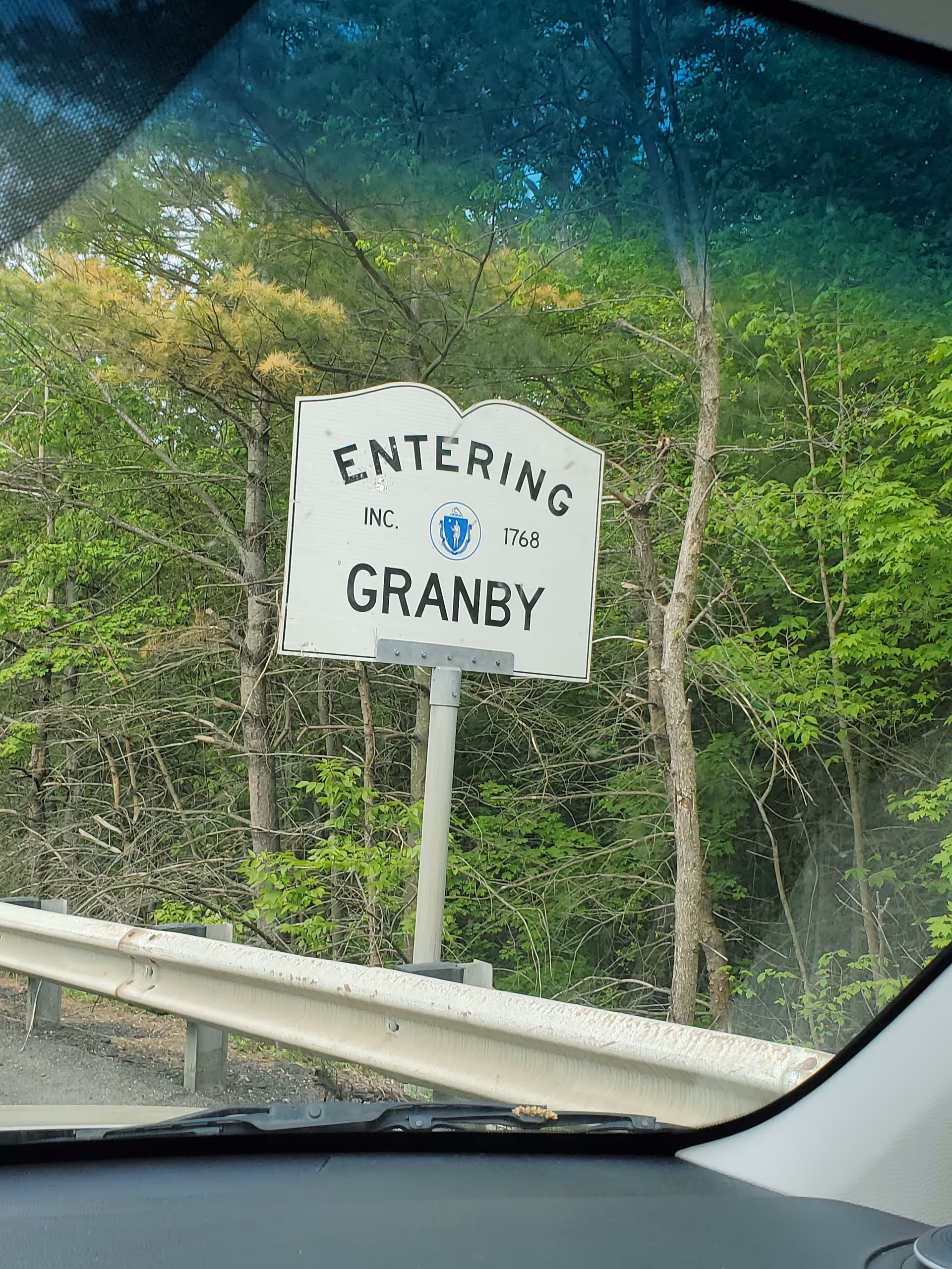 View from a car of an 'Entering Granby' highway sign beside trees.