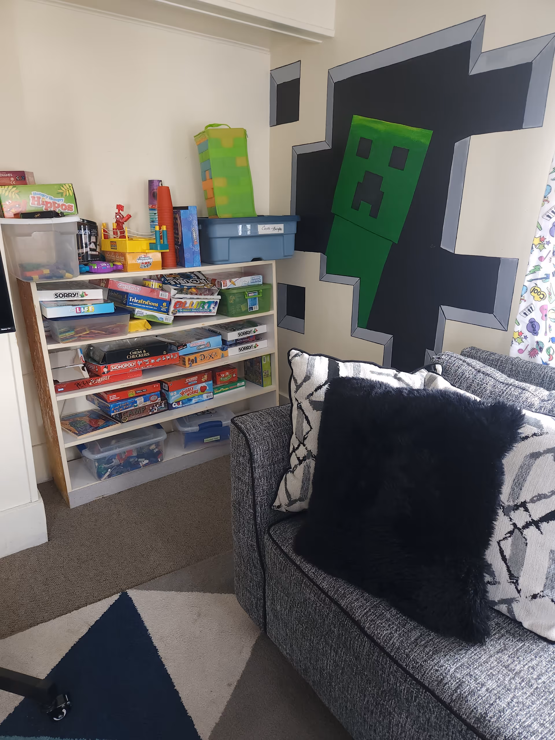 Cozy living room corner with board game shelf, couch, and Minecraft mural.
