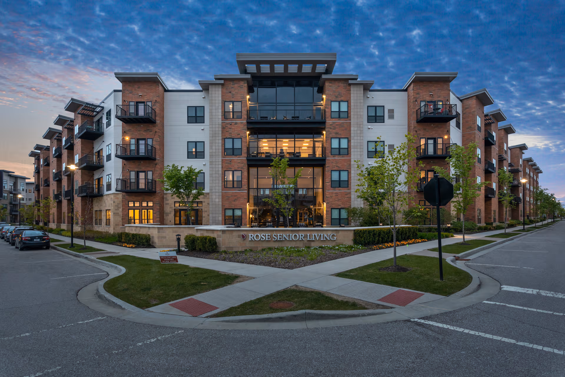 Exterior view of a multi-story brick senior living building with landscaped entrance and sign.
