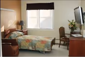 A bright bedroom in a senior living facility with two single beds and a desk.