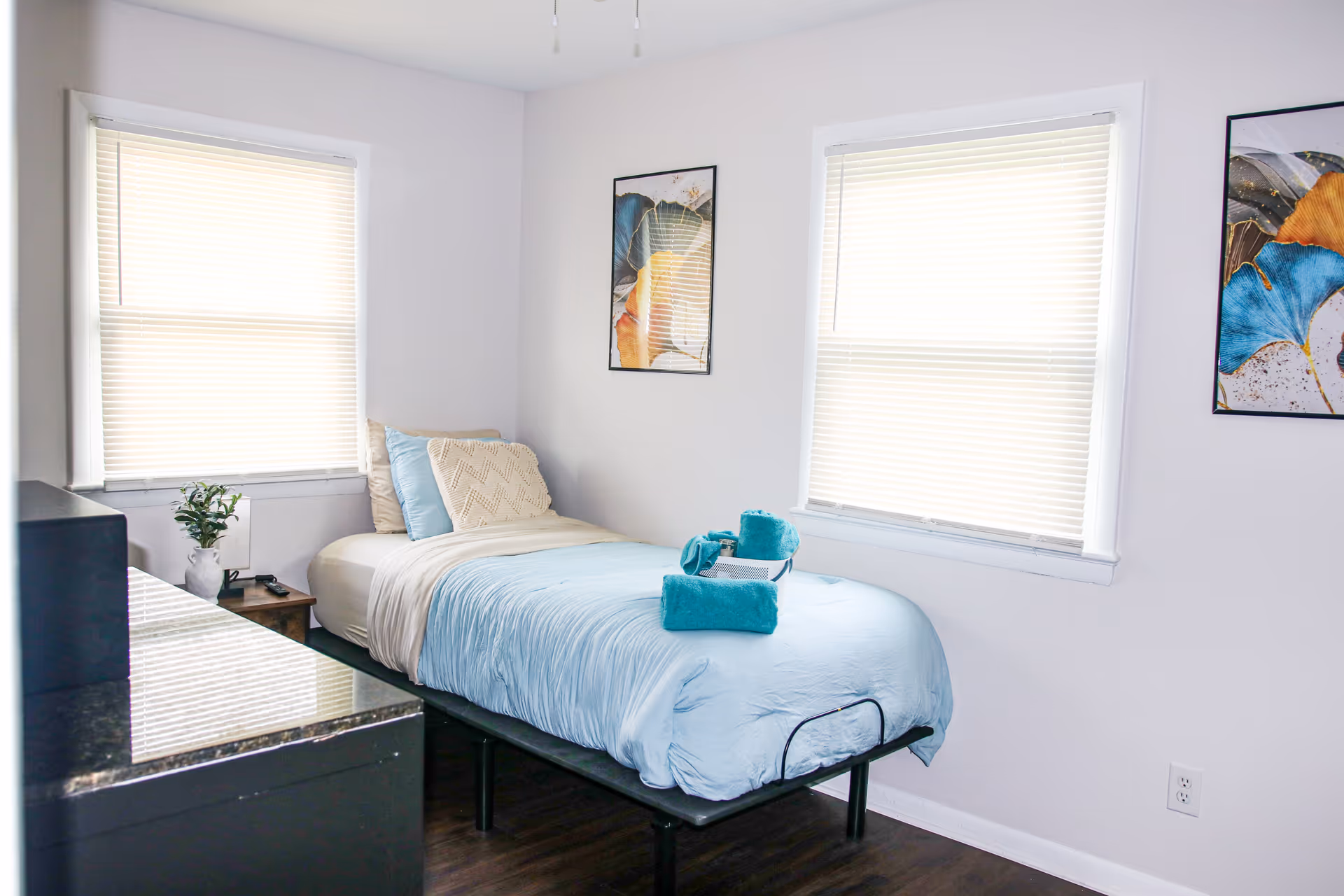 A neatly made bedroom with a single bed, blue bedding, and minimal furnishings.