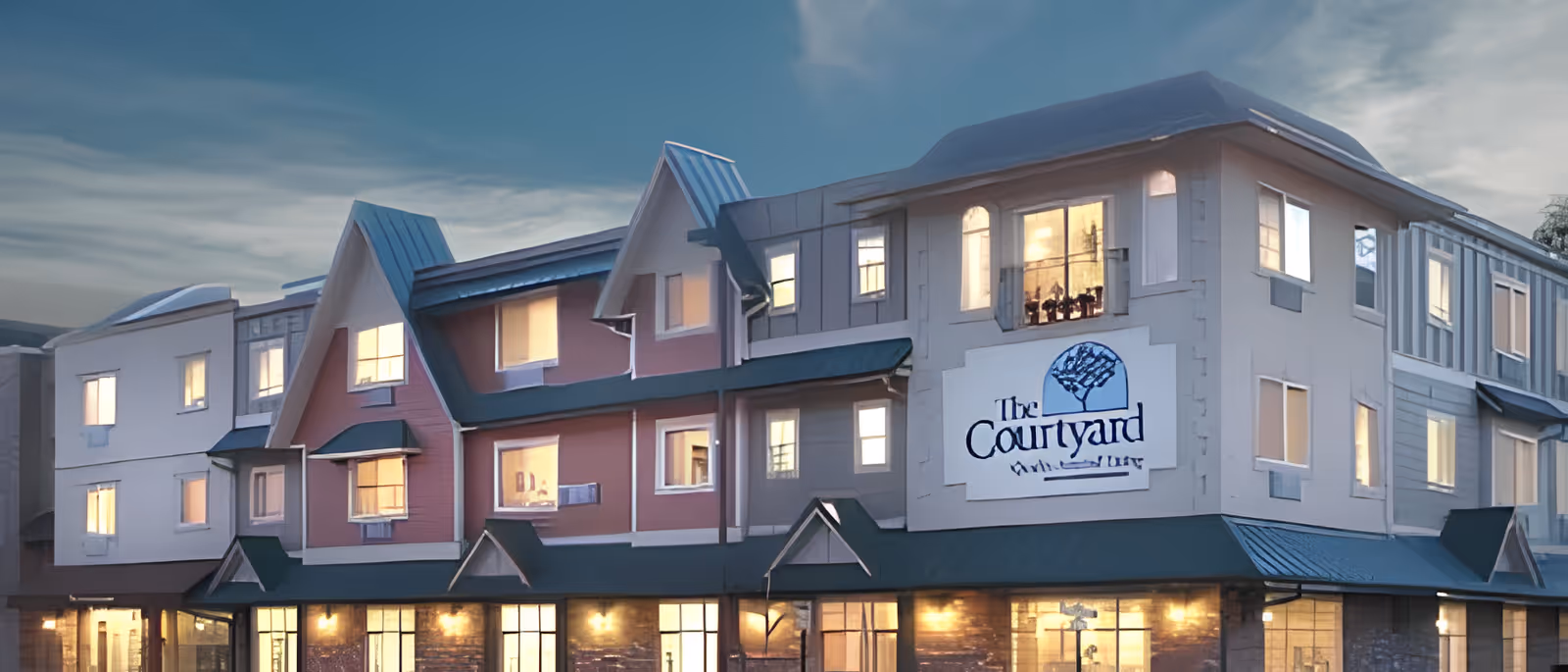 Front facade of a multi-story assisted living building named 'The Courtyard' with lit windows at dusk.