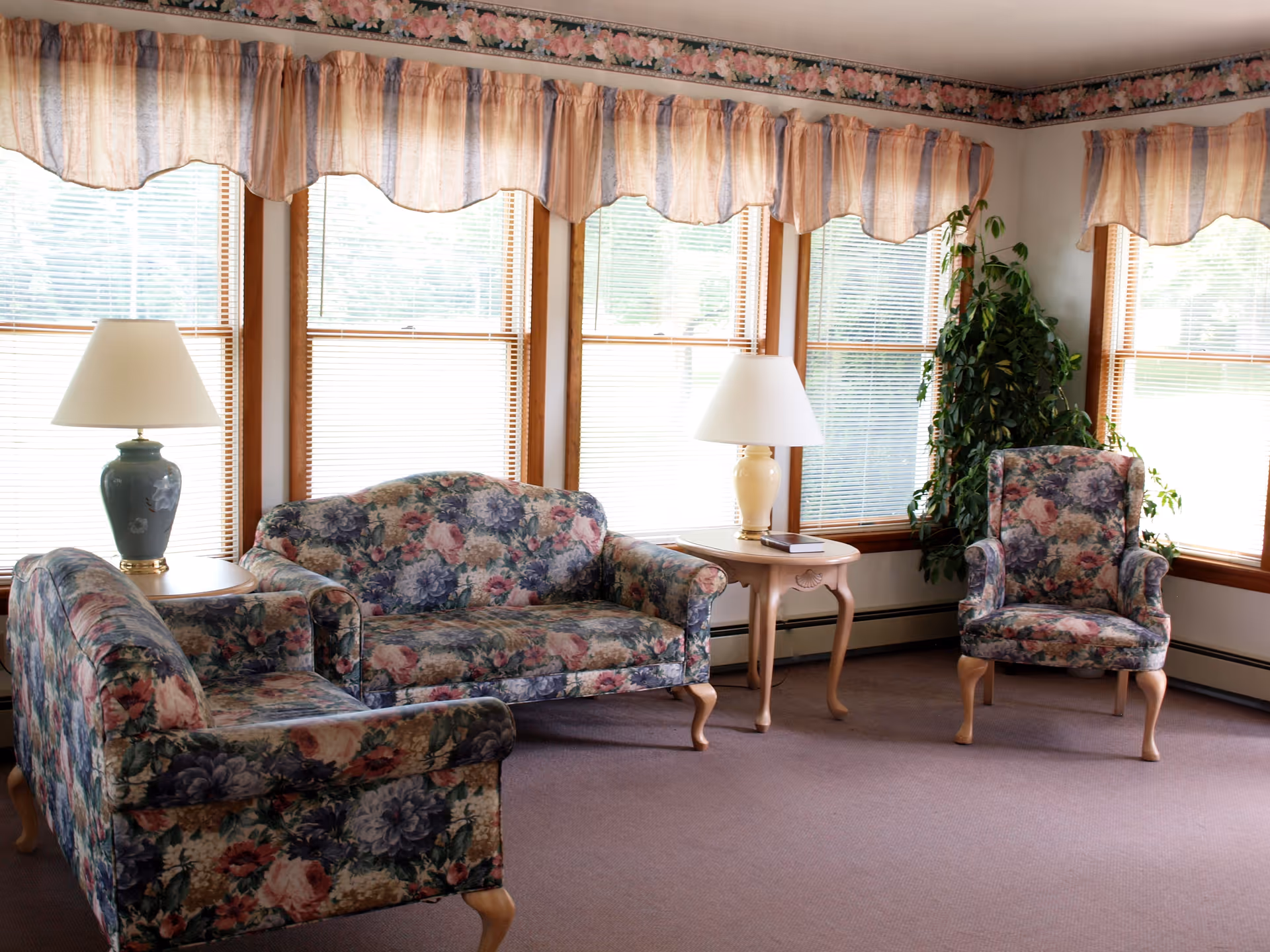 Floral upholstered seating area with lamps and windows in a sunlit living room.