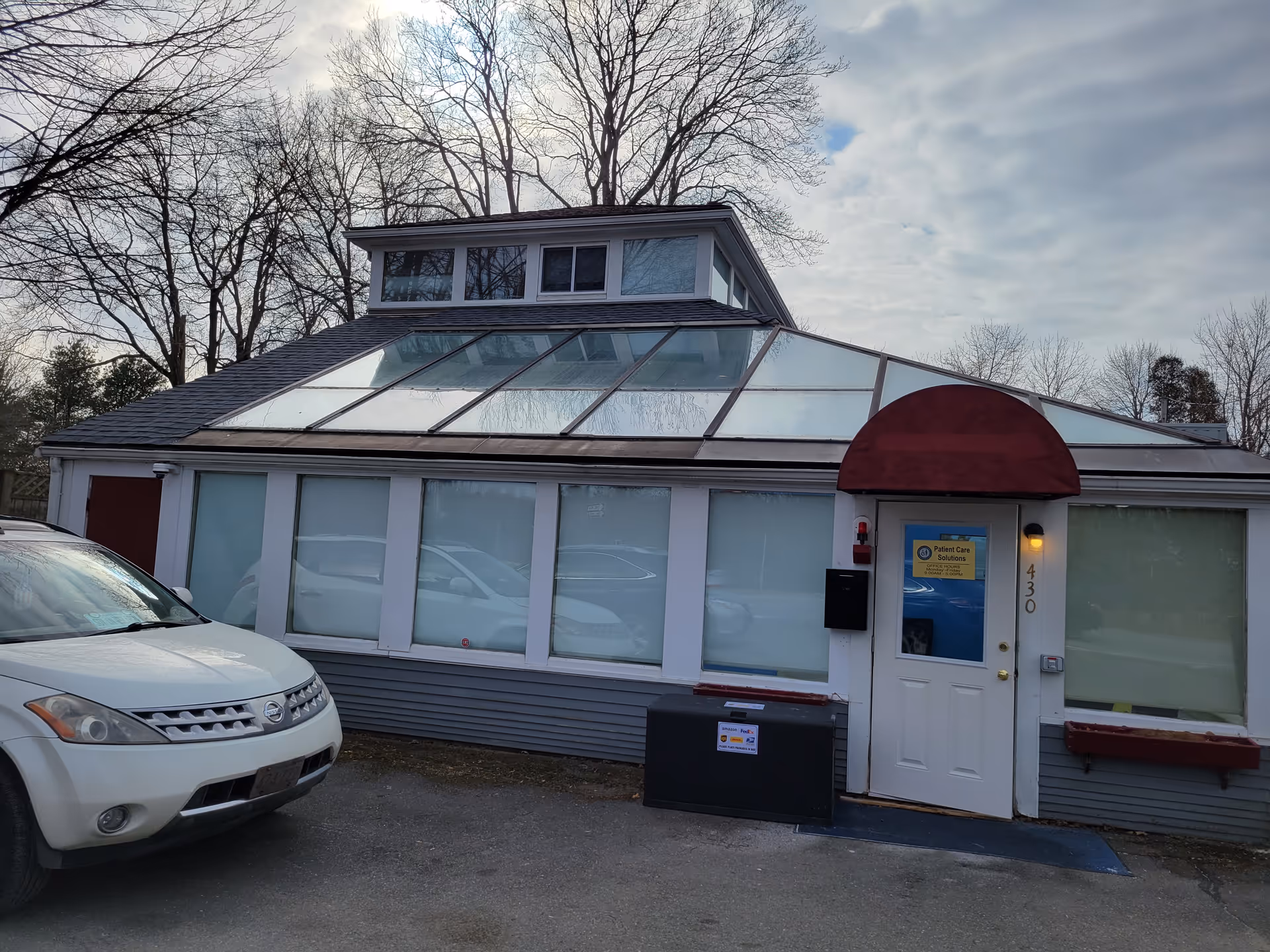 Exterior view of a glass-roofed building with a white door and parked SUV.