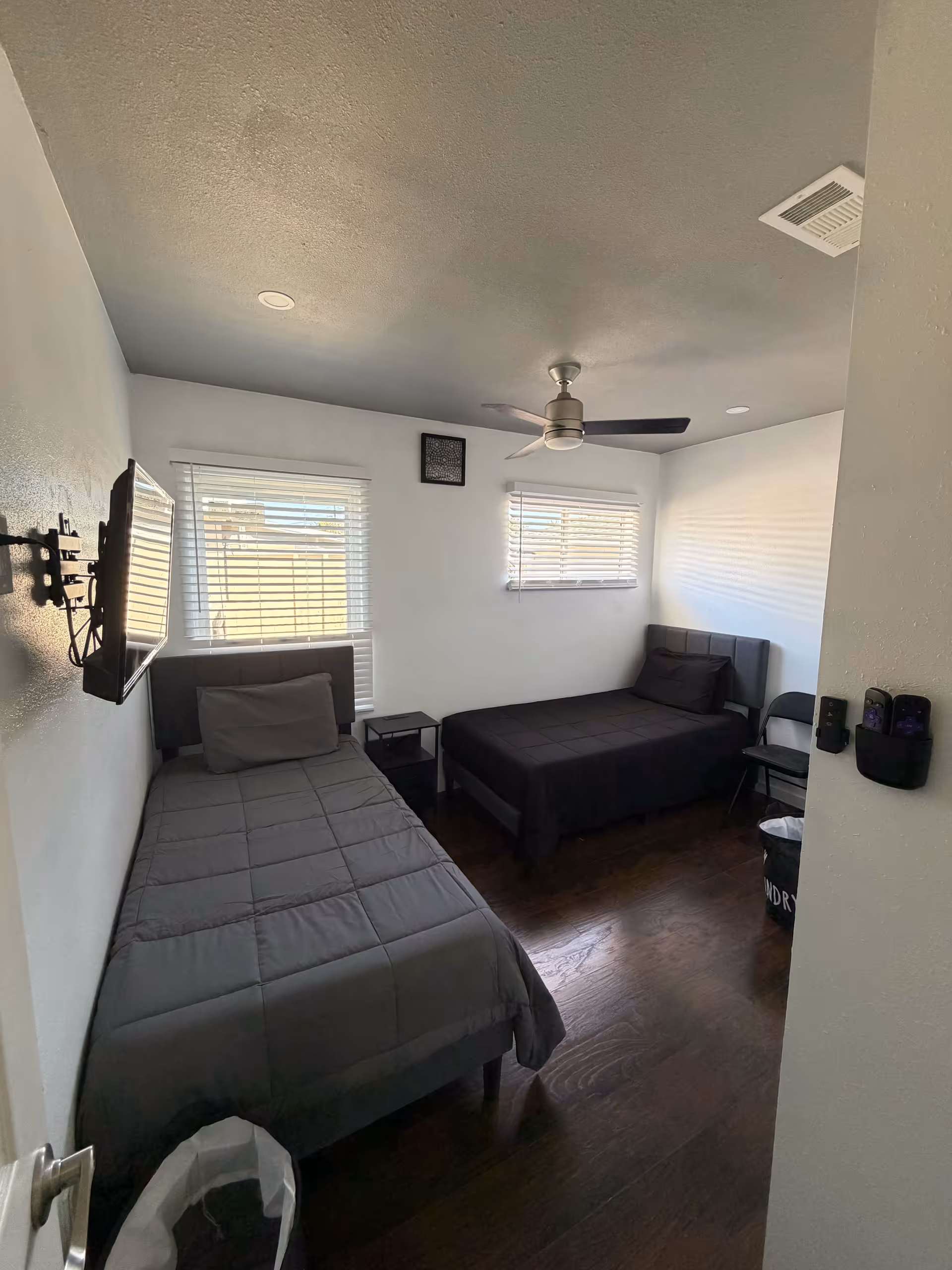 Two twin beds in a small, clean bedroom with windows and ceiling fan