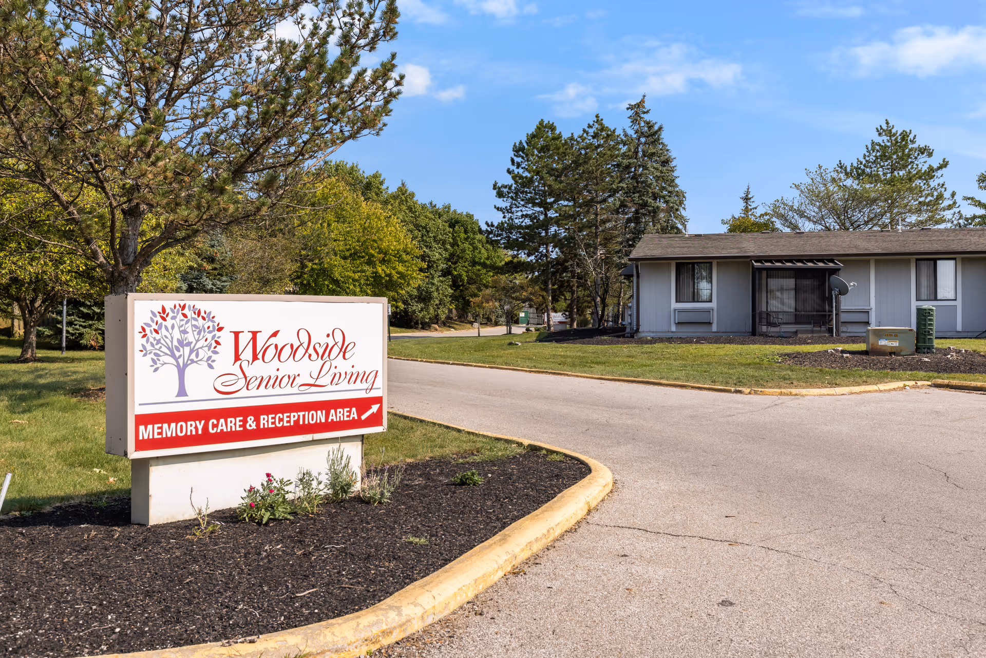 Exterior view of Woodside Senior Living facility featuring a sign and a single-story building.