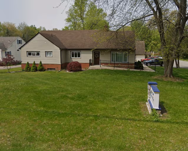 Single-story building with a manicured lawn, shrubs, and a sign in the front yard.