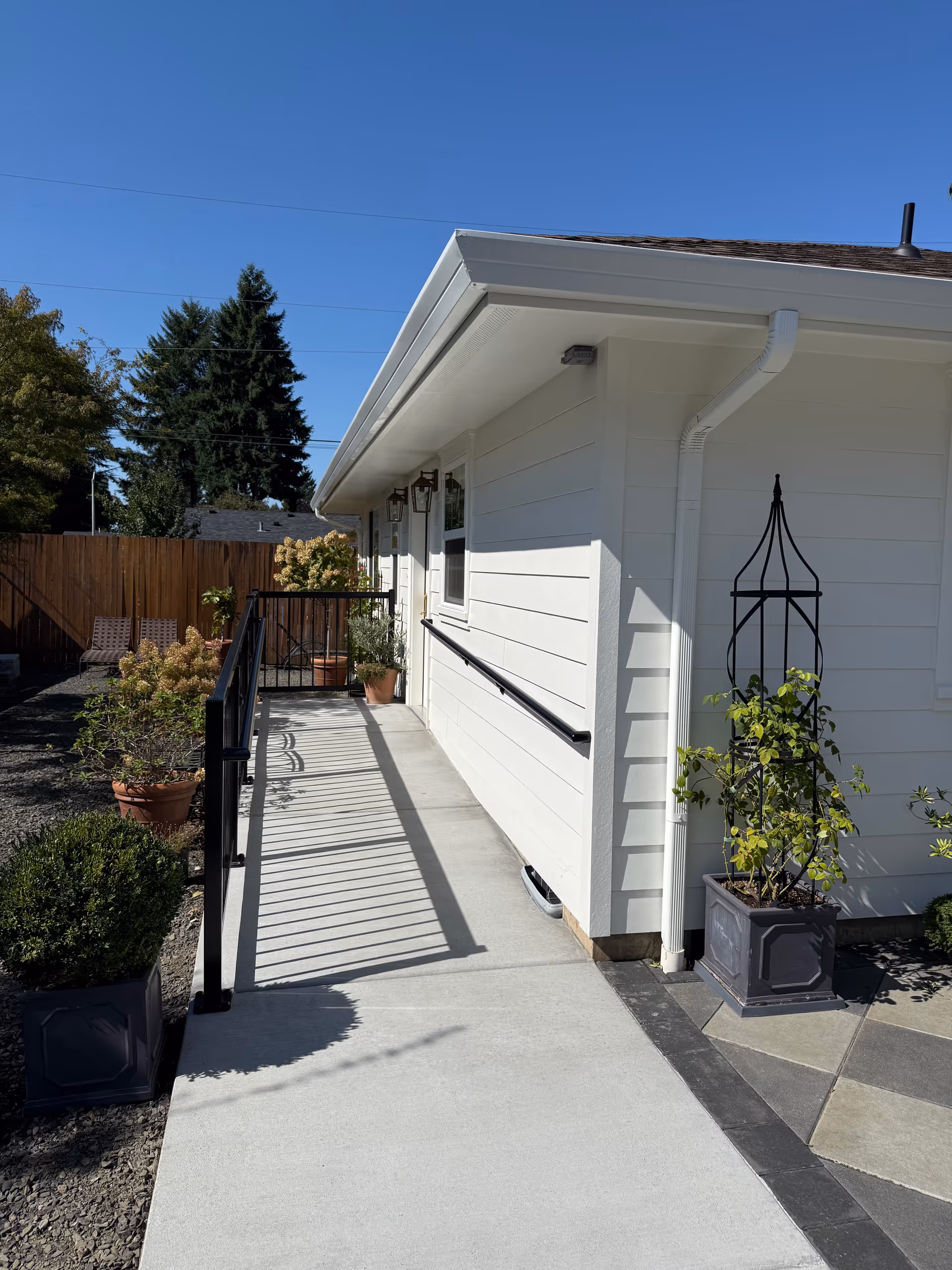 Outdoor entrance of a white senior living facility with a ramp and potted plants.