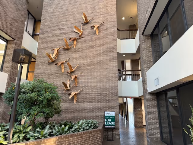 Indoor brick atrium with wall-mounted wooden bird sculptures and balconies.