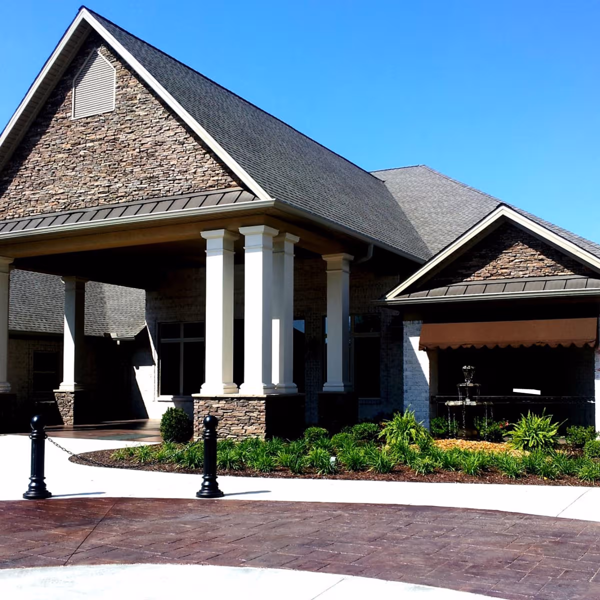 Stone facade senior living facility entrance with columns and landscaped frontage under blue sky